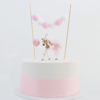 pony cake topper with pink and white pom pom garland